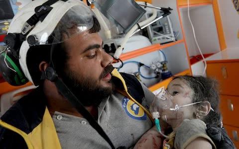 A member of the Syrian civil defence, known as the White Helmets, helps an injured Syrian child after pulling him out from under the rubble  - Credit: OMAR HAJ KADOUR/AFP/Getty Images