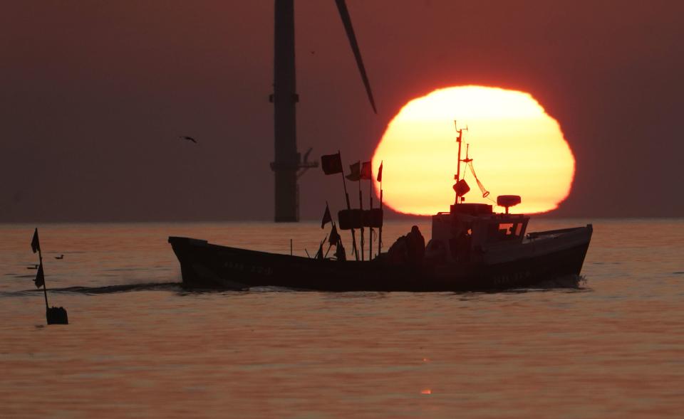 A fishing boat sails in front of the rising sun near Blyth pier in Northumberland (PA)