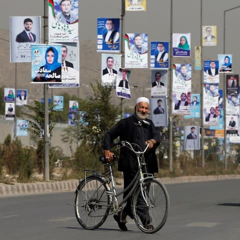 A man walks with his bicycle in front of election posters of parliamentary candidates during the first day of election campaign in Kabul - Credit: Omar Sobhani/Reuters