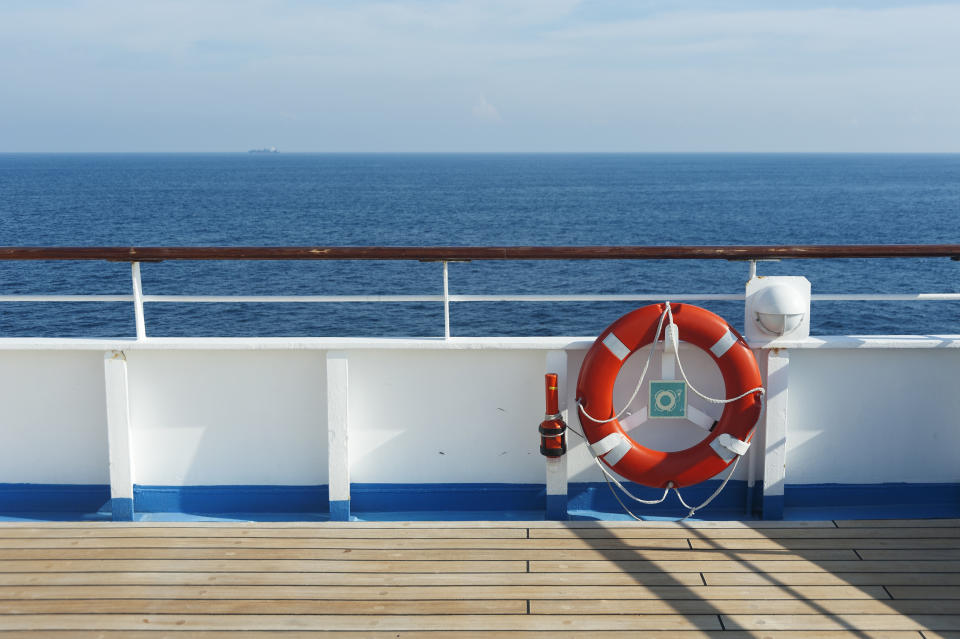 A lifebuoy is attached to the railing of a ship's deck, with the ocean visible in the background