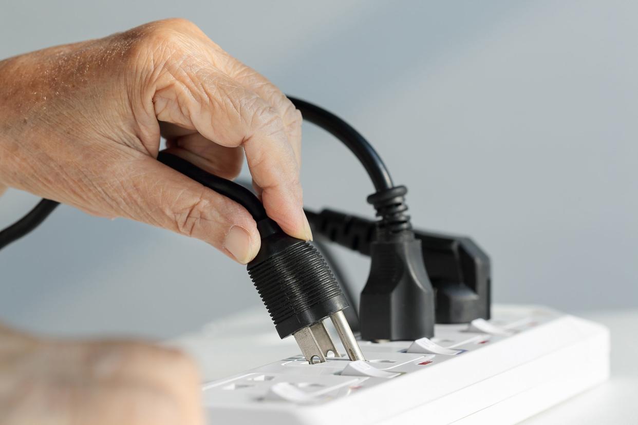 close up elderly hand unplugging into electrical outlet