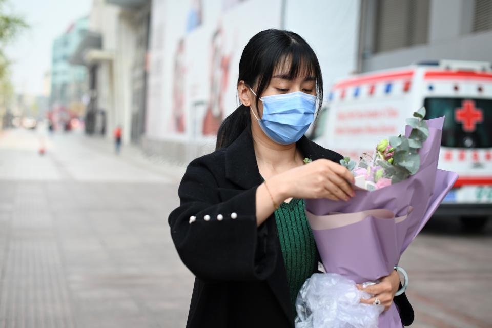 A woman wearing a face mask, amid concerns of the COVID-19 coronavirus, looks carries a bunch of flower as she walks along a road in Beijing on March 31, 2020. (Photo by WANG ZHAO / AFP) (Photo by WANG ZHAO/AFP via Getty Images)