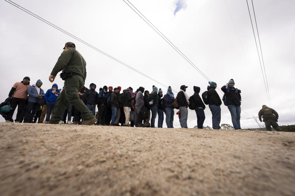 Men seeking asylum, including Peruvians, line up as they wait to be processed after crossing the border with Mexico nearby, Thursday, April 25, 2024, in Boulevard, Calif. Mexico has begun requiring visas for Peruvians in response to a major influx of migrants from the South American country. The move follows identical ones for Venezuelans, Ecuadorians and Brazilians, effectively eliminating the option of flying to a Mexican city near the U.S. border. (AP Photo/Gregory Bull)