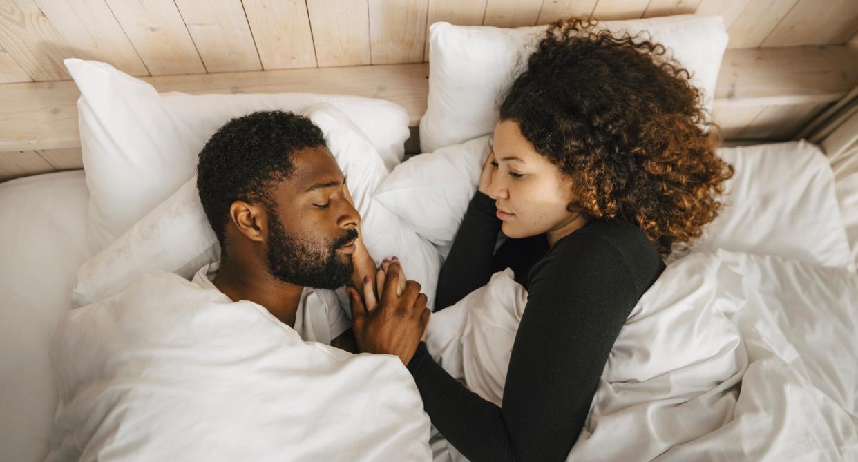 Man sleeps in bed while woman looks on and cradles his face. (Getty Images)