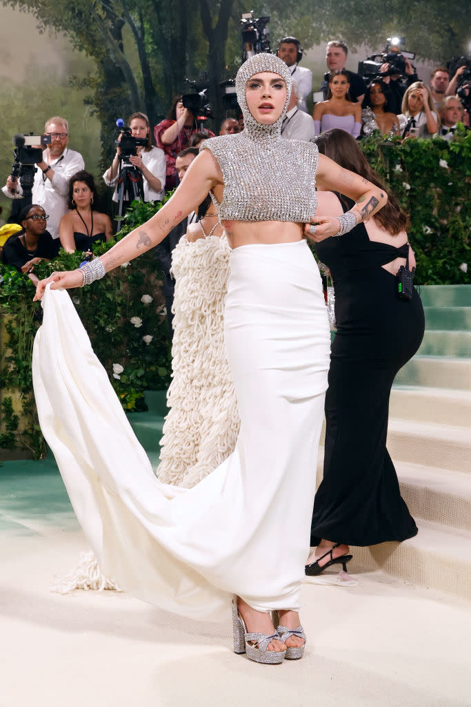 Woman posing on the staircase in a chainmail crop top with a white skirt and train, accessorized with a headpiece