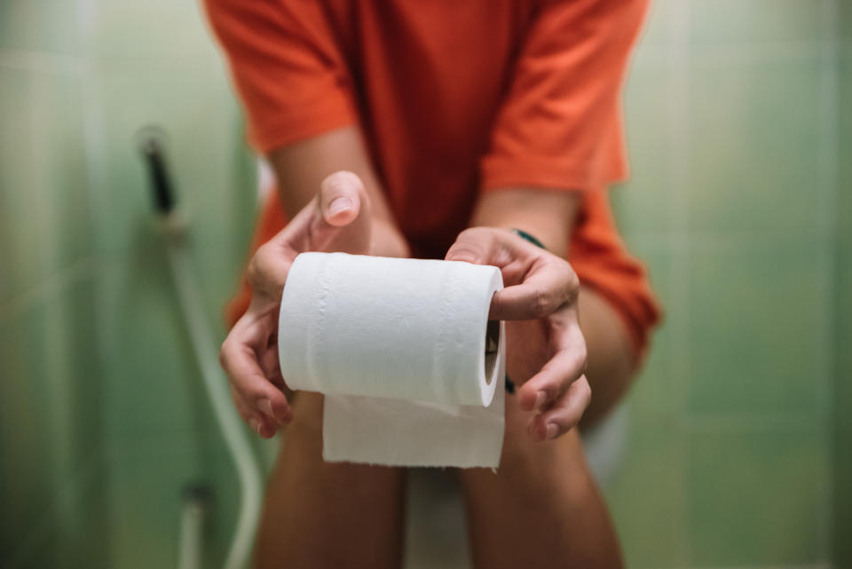 Person sitting on a toilet holding a roll of toilet paper