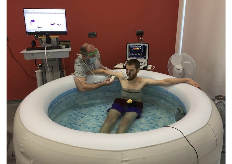 Man hooked up to medical equipment sits in hot tub.