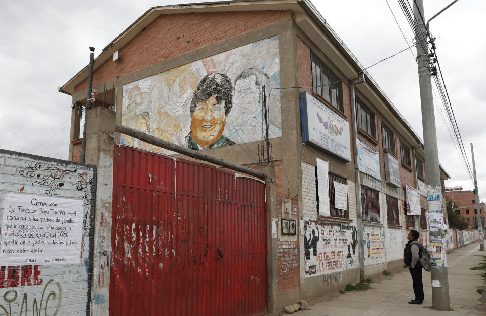 In this Jan. 18, 2020 photo, a man looks at a mural of Bolivia's former President Evo Morales painted on a wall of the Republic of Russia school in El Alto, Bolivia. While attempting to erase the images and statues of hated former leaders is often greeted by broad social consensus in other countries, it is facing backlash in Bolivia where Morales still has supporters, especially among indigenous peoples. (AP Photo/Juan Karita)