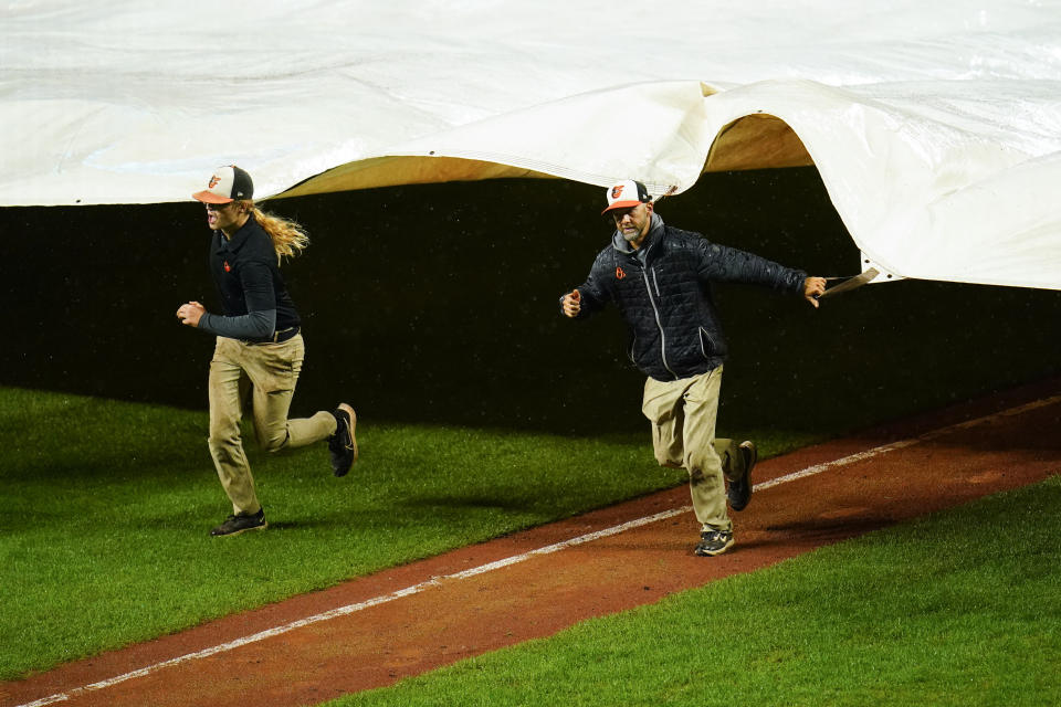 Grounds crew members place a tarp over the infield at Oriole Park at Camden Yards during a rain delay in the eighth inning of a baseball game between the Baltimore Orioles and the Toronto Blue Jays, Monday, Oct. 3, 2022, in Baltimore. (AP Photo/Julio Cortez)