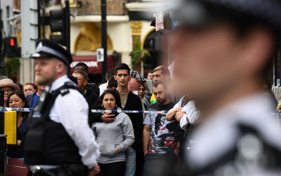 Members of the public stand beyond a cordon as police officers stand on duty outside a row of shop, with residential flats above, in East Ham - Credit:  JUSTIN TALLIS