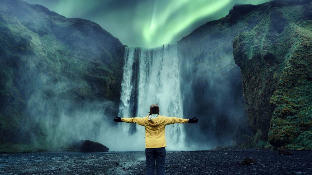 aurora borealis over skogafoss waterfall and cheerful tourist woman standing in travel famous place on summer in iceland