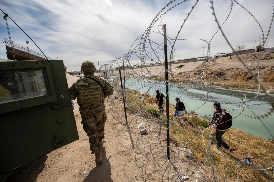 Colombian migrants walk on the U.S. side of the Rio Grande as a Texas National Guard officer explains to them that they must make an entry at a port of entry. 