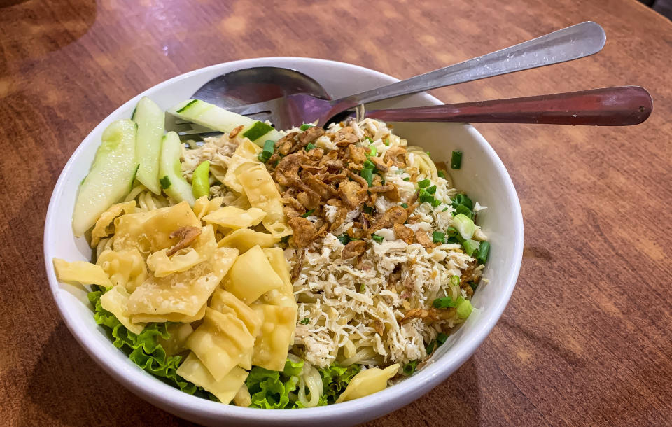 white bowl with large fried wontons, cucumbers and metal spoon and fork