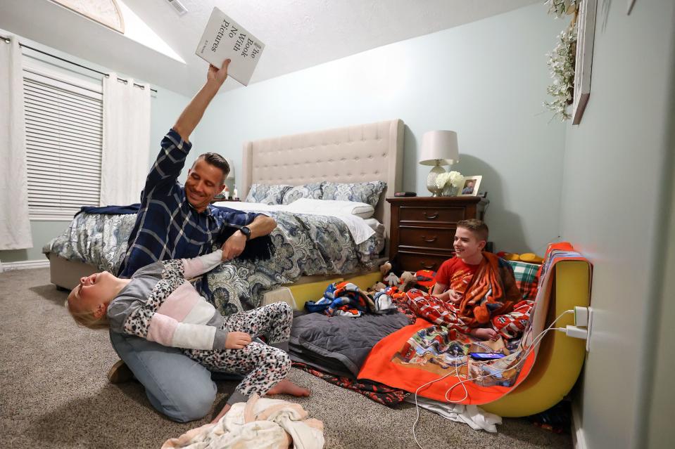 Kyle Sintz jokes around with his daughter Chloe Sintz as they read a bedtime story as Isaac Sintz listens and watches from his bed at home in South Jordan on Wednesday, March 22, 2023. Isaac, 16, has Dravet Syndrome. He shares a bedroom with his parents due to his seizures that sometimes happen in the middle of the night. | Kristin Murphy, Deseret News