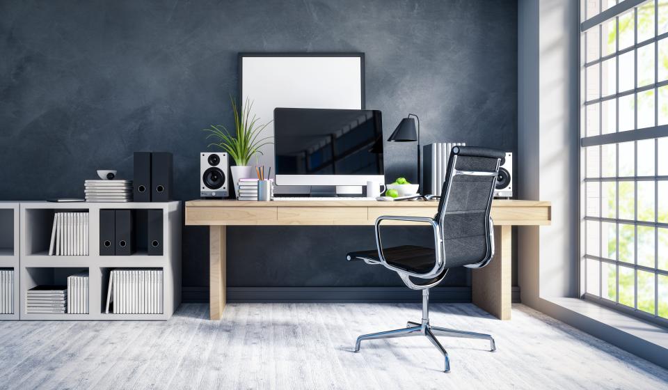 A home office space with a MacBook, speaker, and dry era board atop a desk that has a window on the right and a shelving unit on the left