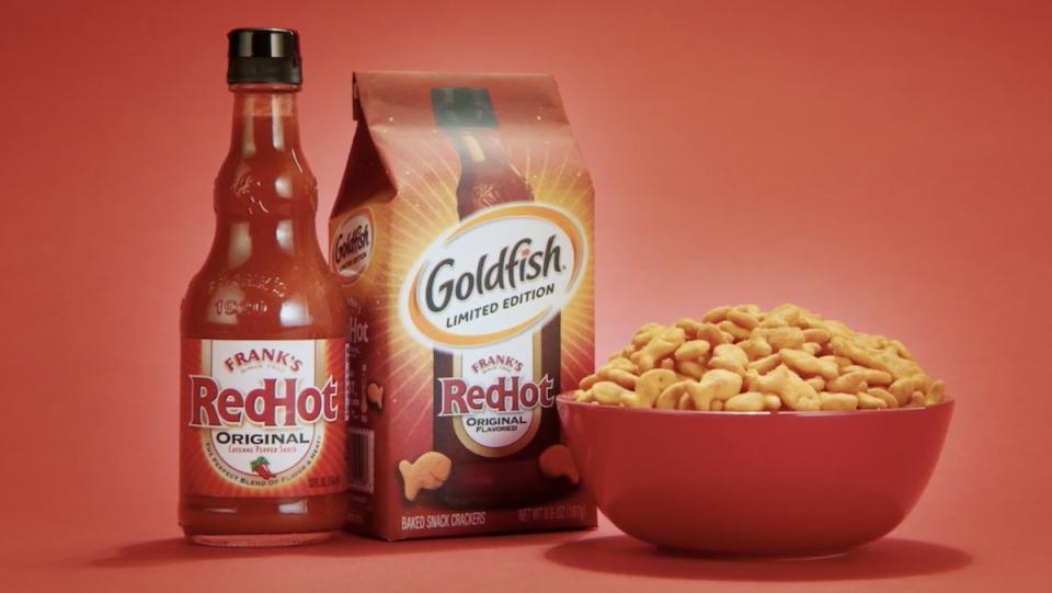 A bottle of Frank's RedHot sauce, a bag of Goldfish, and a bowl of Goldfish