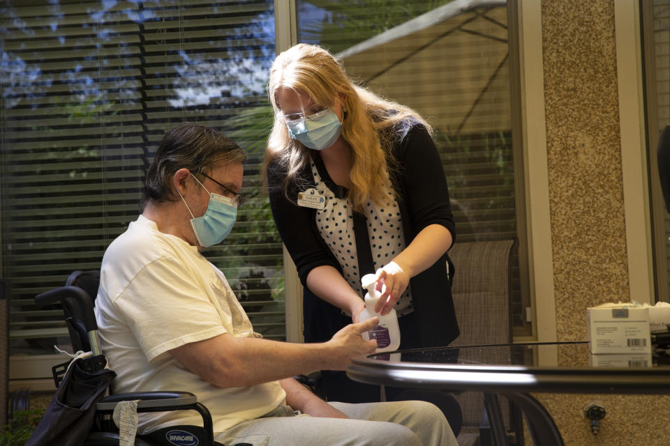 KIRKLAND, WA - AUGUST 24: Sarah Tongson (R), Director of Social Services, gives Douglas Smith some hand santizer during a visit with his wife Deborah Trigueiro at the Life Care Center of Kirkland on August 24, 2020 in Kirkland, Washington. This is only the second time Smith and his wife have seen each other in person since February when the coronavirus (COVID-19) raced through the facility. Prior to their first visit last week they had to talk through the window on a phone. Recently, Washington state Governor Jay Inslee issued a directive to allow visitors to long-term care facilities. The families cannot touch, must visit outside and stay socially distant. The Life Care Center of Kirkland, a nursing home, was an early epicenter for coronavirus outbreaks in the U.S. According to a report by the CDC, at least 37 coronavirus deaths have been linked to this facility. Prior to (Photo by Karen Ducey/Getty Images)