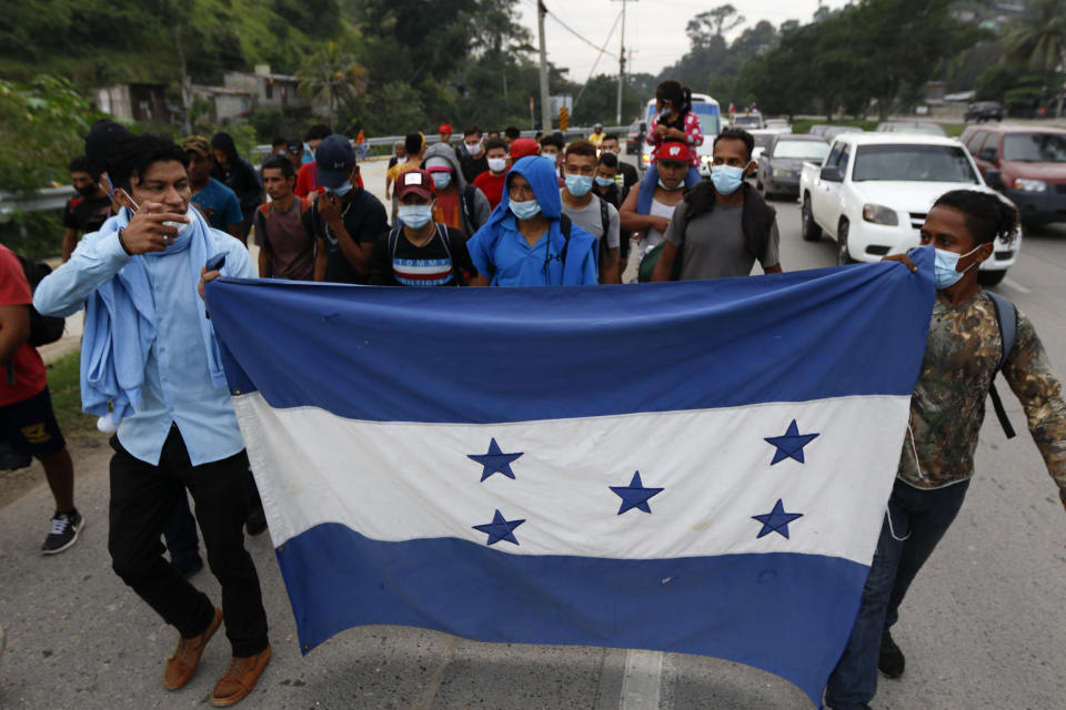 Migrantes que intentan llegar a Estados Unidos caminan el jueves 14 de enero de 2021 con la bandera hondureña, en Choloma, Honduras. (AP Foto/Delmer Martínez)