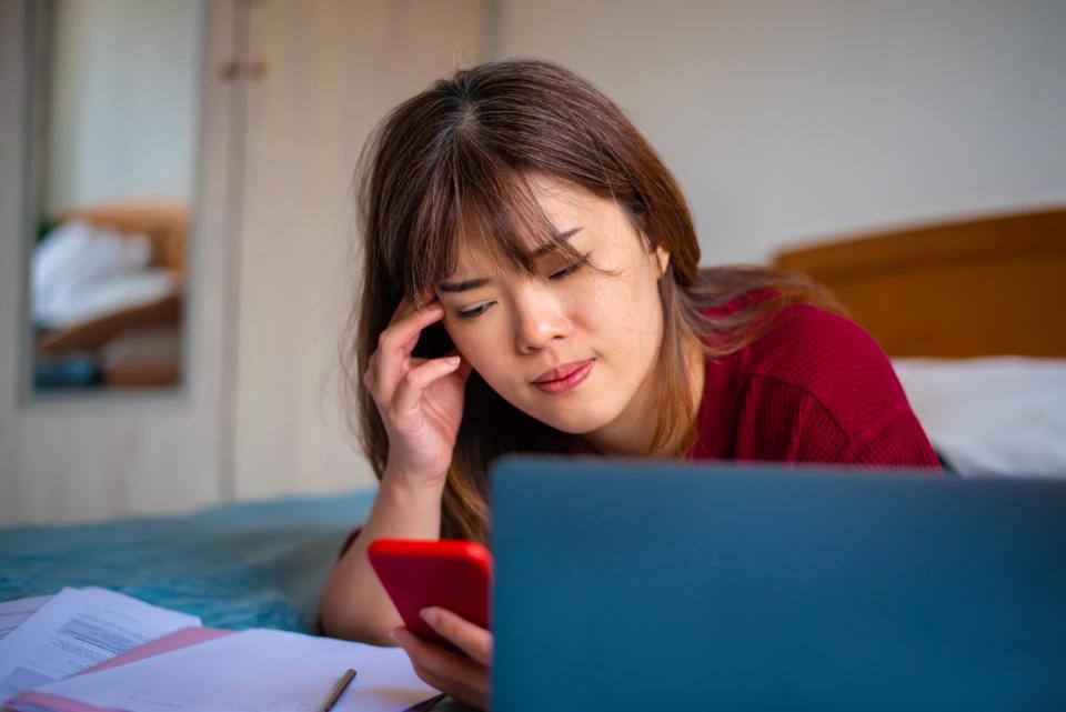 A stressed Asian woman frowns while looking at her mobile phone.