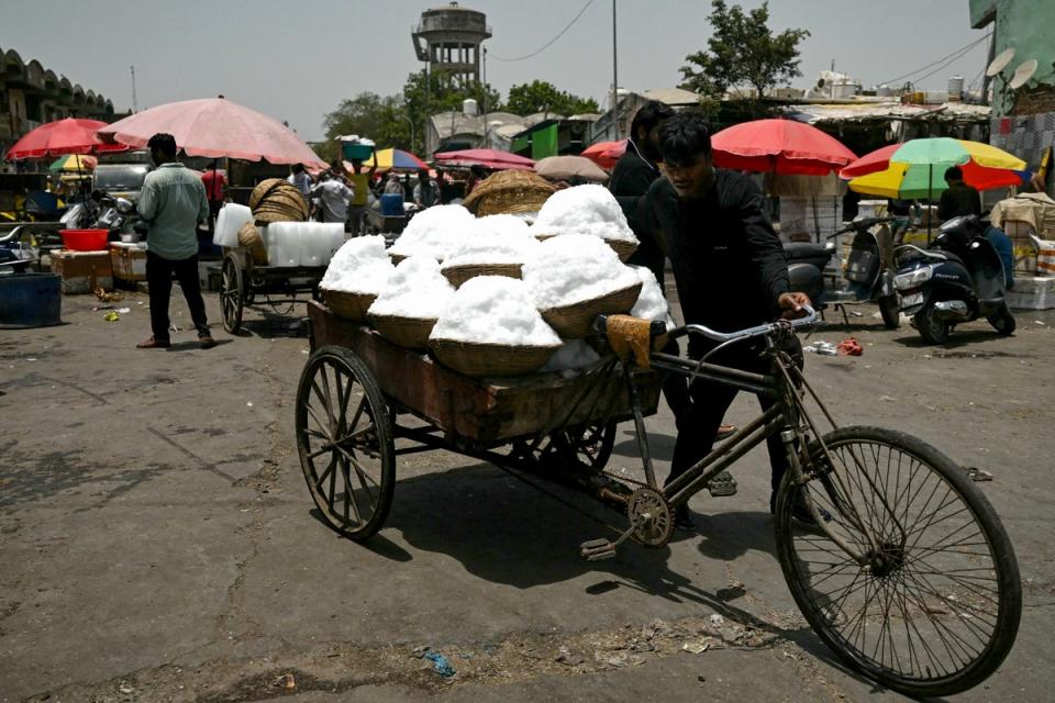 A worker carries baskets of shaved ice to a food processing unit on a hot summer afternoon, at a market in Delhi (AFP via Getty Images)
