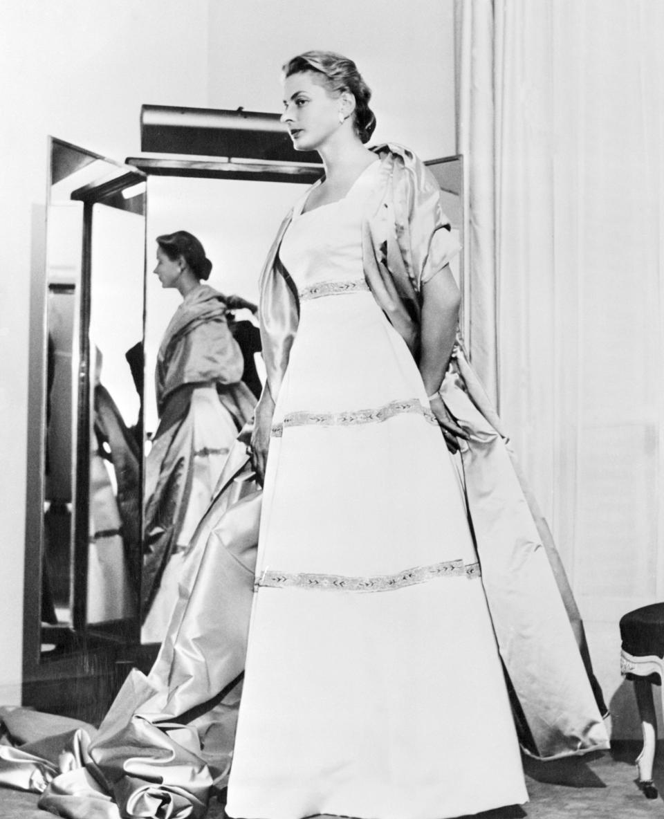 (Original Caption) Ingrid Models Anastasia Wardrobe. London, England: Actress Ingrid Bergman, wife of Italian director Roberto Rossellini, in costumes created for her in the title role of the 20th Century fox film, Anastasia, now being filmed in London. The costumes were designed by M. Hubert. At left, the evening dress worn by Miss Bergman as Anastasia in a scene at the Royal Opera House in Copenhagen is a Balenciaga model in princess style, of white satin armure (slipper satin) embroidered with bands of white and pink beads going completely around the skirt in a watteau motif. Center, for the scene in which Miss Bergman meets members of Paris' White Russian colony for the first time, she wears this black afternoon dress in simple lines of the 1928 period. The dress has the new look of 1957 fashions. The material is silk and wool with linen thread. There is no belt and almost