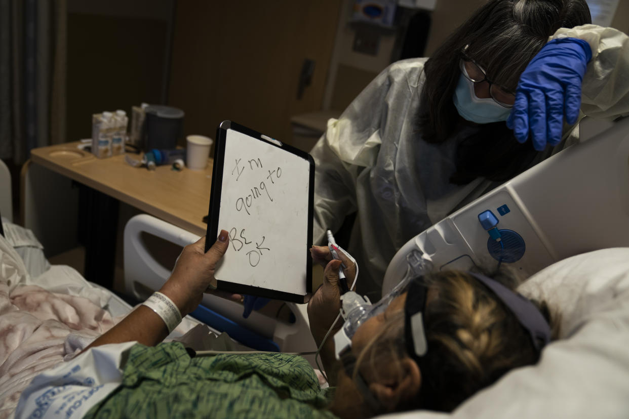 Mary Lou Samora, a 71-year-old COVID-19 patient, writes on a white board, "I'm going to be OK," while using the board to communicate with her long time friend, Becky Gonzalez, 67, at Providence Holy Cross Medical Center in Los Angeles, Friday, Dec. 17, 2021. (AP Photo/Jae C. Hong)