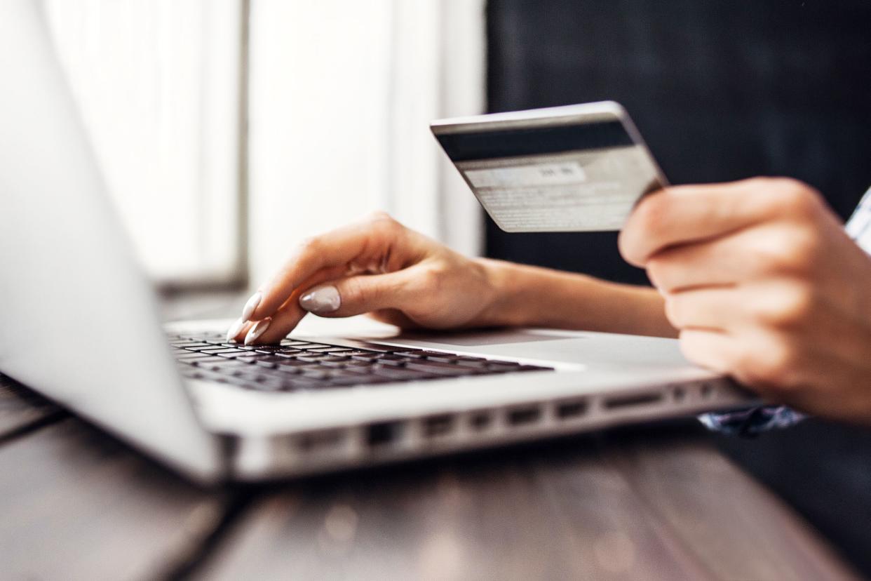 Closeup of laptop on table and hands holding a credit card by window, semi-blurred background