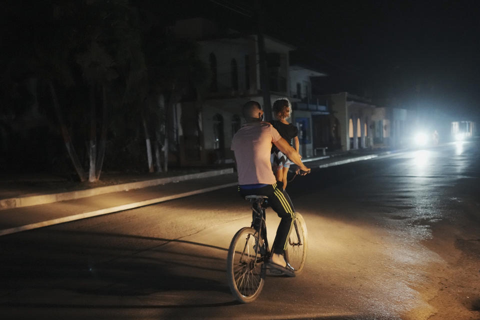 Un hombre pedalea en su bicicleta llevando a una niña durante el apagón programado de electricidad en Bauta, Cuba, el lunes 18 de marzo de 2024. La isla enfrenta una crisis de energía, con varios apagones en las últimas semanas. (AP Foto/Ramón Espinosa)