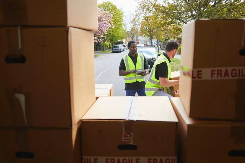 Two removal men carrying boxes. View point is from inside the removals van, amongst boxes.