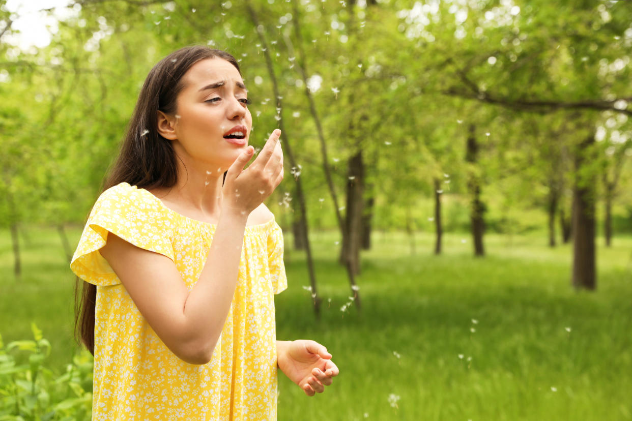 Woman standing outdoors amidst pollen about to sneeze