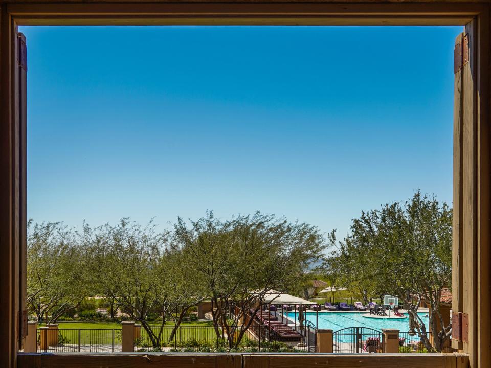 A pool and a grass courtyard seen from an open wooden window