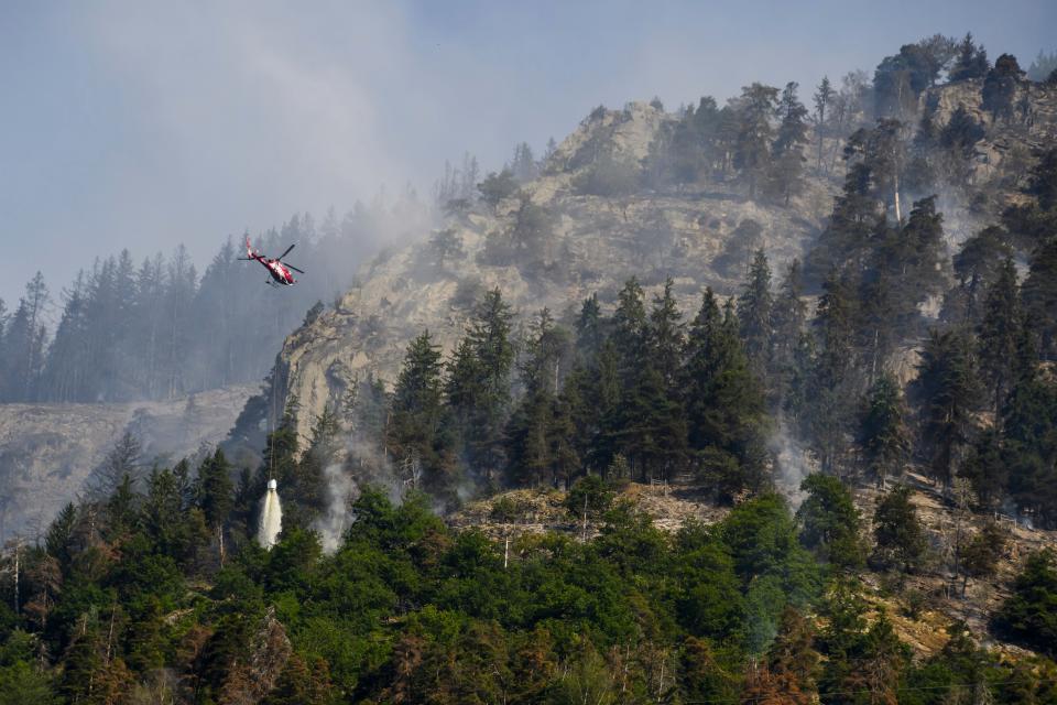 A helicopter drops water on forests on fire above the communes of Bitsch and Ried-Moerel, in Bitsch, Switzerland, on July 18, 2023.