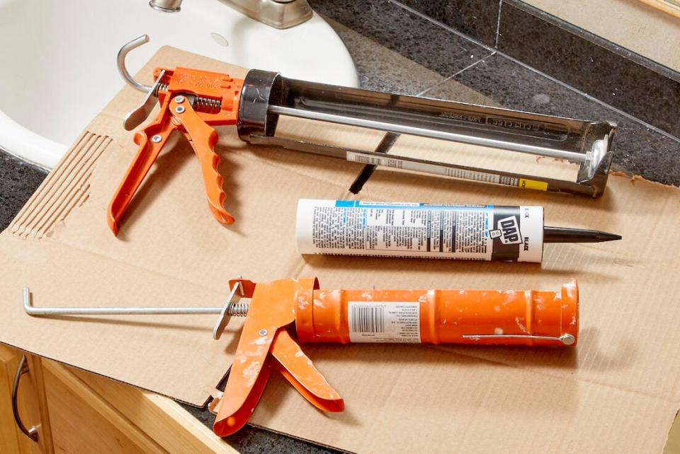 Caulk guns and caulk tube on top of a piece of cardboard on a bathroom vanity.