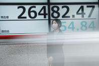 A woman wearing a protective face mask to help curb the spread of the coronavirus stands near an electronic stock board showing Japan's Nikkei 225 index at a securities firm as a car passing by Friday, Nov. 27, 2020, in Tokyo. Asian stock markets declined Friday as questions about the effectiveness of one possible coronavirus vaccine weighed on investor optimism. (AP Photo/Eugene Hoshiko)