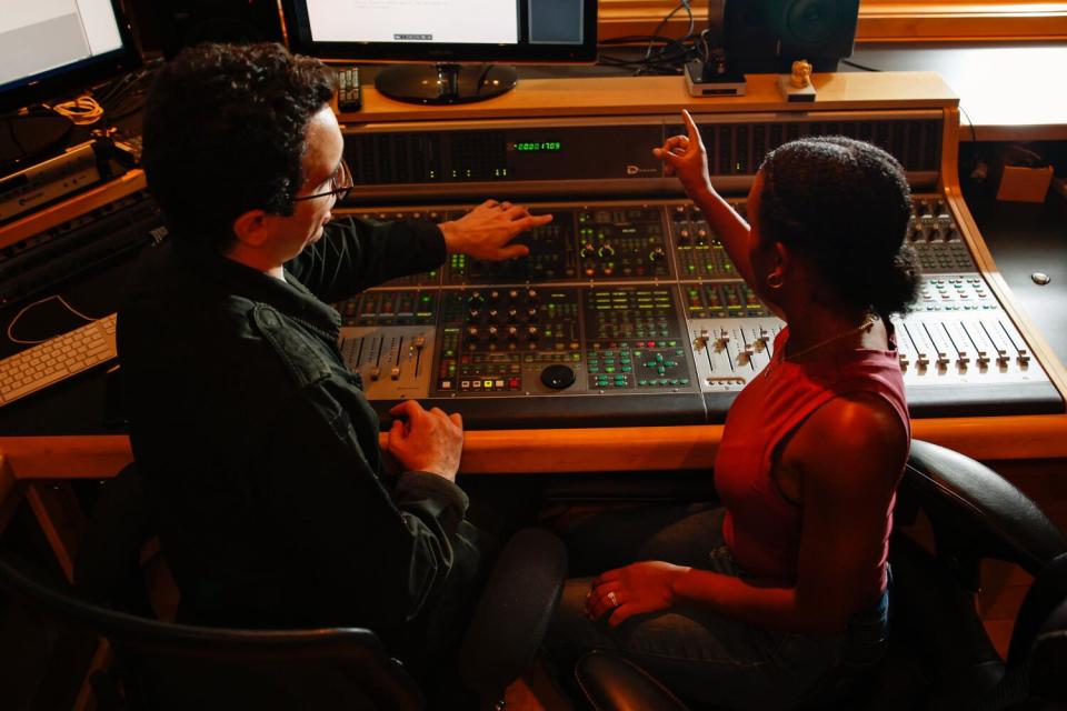 A man points at a mixer board as he and a woman talk
