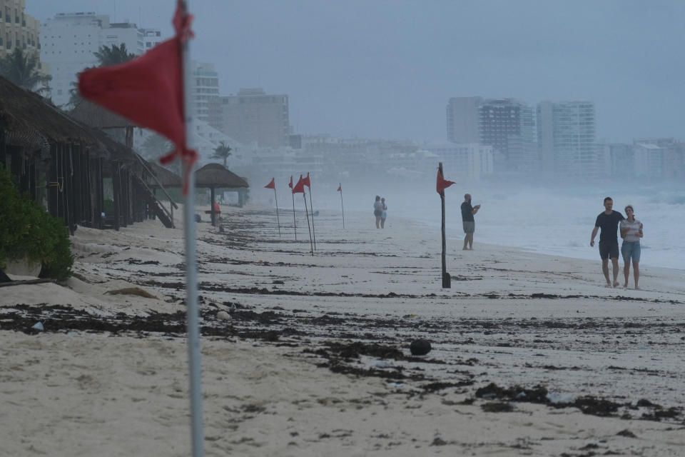 People walk past red flags warning beachgoers of dangerous conditions as Tropical Storm Helene approaches the Yucatan Peninsula, in Cancun, Mexico, Tuesday. (Paola Chiomante/Reuters)