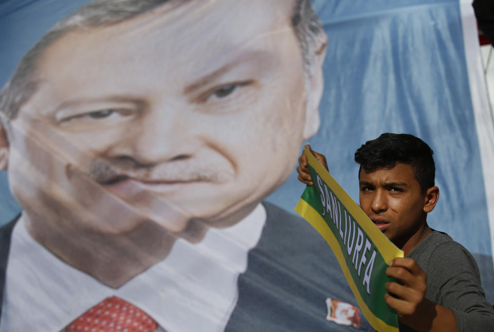 A poster of Turkey's President Recep Tayyip Erdogan is held up during show of support by about a dozen people for Turkey's operation in Syria, in the border town of Akcakale, Sanliurfa province, southeastern Turkey, on Monday, Oct. 14, 2019. Erdogan has criticized NATO allies which are looking to broaden an arms embargo against Turkey over its push into northern Syria. (AP Photo/Lefteris Pitarakis)