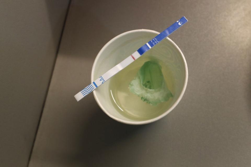 A test strip rests atop a cup of clear liquid with a green substance