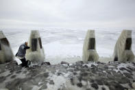 In this image taken Thursday Feb. 9, 2012, A tourist climbs onto the frozen IJsselmeer inland sea on Afsluitdijk, a dike closing off the Wadden sea and North Sea from IJsselmeer inland sea, northern Netherlands. Rising in a thin line through the surface of waters separating the provinces of North Holland and Friesland, the 87-year-old Afsluitdijk is one of the low-lying Netherlands' key defenses against the sea. With climate change bringing more powerful storms and rising sea levels, it's getting a major makeover. (AP Photo/Peter Dejong)