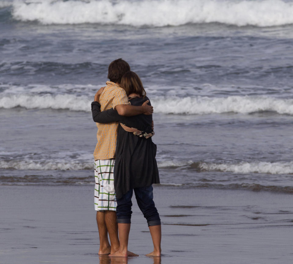 Meg Strange, right, wife of Adam Strange is comforted by friend Simon Shephard, as people gather on Muriwai Beach near Auckland, New Zealand, Thursday, Feb. 28, 2013, to say goodbye to Adam Strange. About 150 friends and family of Adam, 46, wrote messages to him in the sand and stepped into the water Thursday at a New Zealand beach to say goodbye after he was killed Wednesday by a large shark. (AP Photo/New Zealand Herald, Brett Phibbs) New Zealand Out, Australia Out