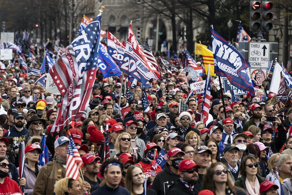 A crowd of Trump supporters wave Trump flags and wear red hats.