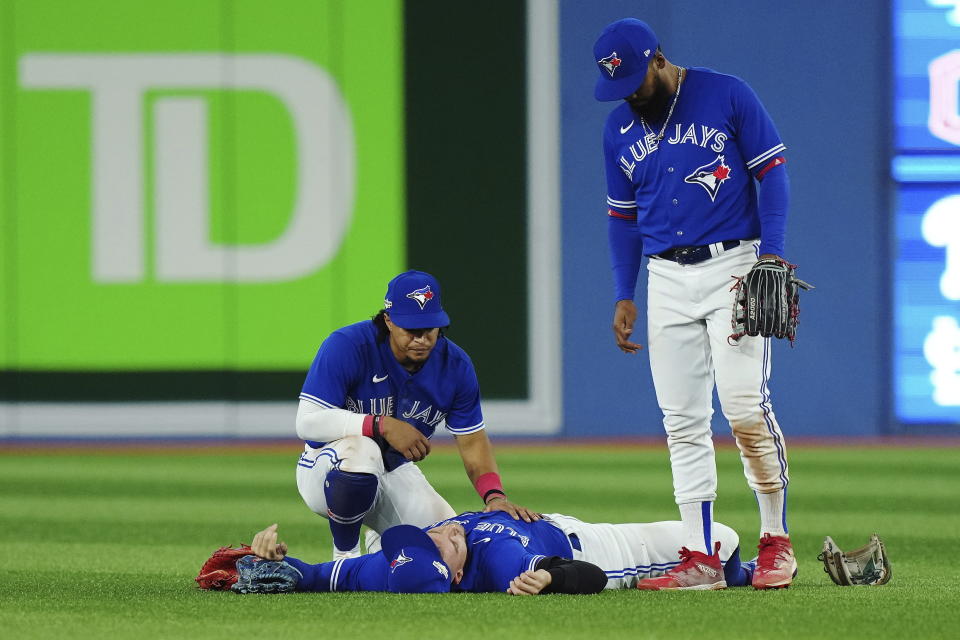 Toronto Blue Jays center fielder George Springer, lays on the field after being injured on a three-RBI double off the bat of Seattle Mariners shortstop J.P. Crawford as Santiago Espinal, left, and Teoscar Hernandez look on during the eighth inning of Game 2 of a baseball AL wild-card playoff series, Saturday, Oct. 8, 2022, in Toronto. (Nathan Denette/The Canadian Press via AP)
