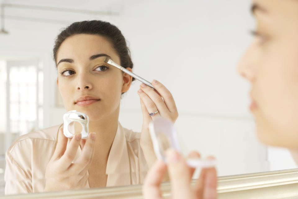 A woman applies makeup in the mirror.