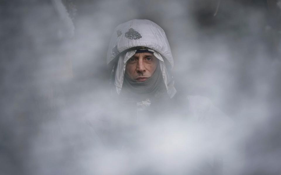 A Ukrainian serviceman, seen through a camouflage mesh, stands at a frontline position in the Luhansk region, eastern Ukraine - Vadim Ghirda/AP