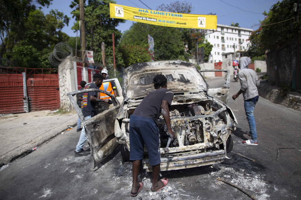 People try to recover usable material from a burned-out car during a protest a day after the murder of President Jovenel Moise, in Port-au-Prince, Haiti, Thursday, July 8, 2021. Moise was assassinated after a group of armed men attacked his private residence, and gravely wounding his wife, First Lady Martine Moise. (AP Photo/Joseph Odelyn)