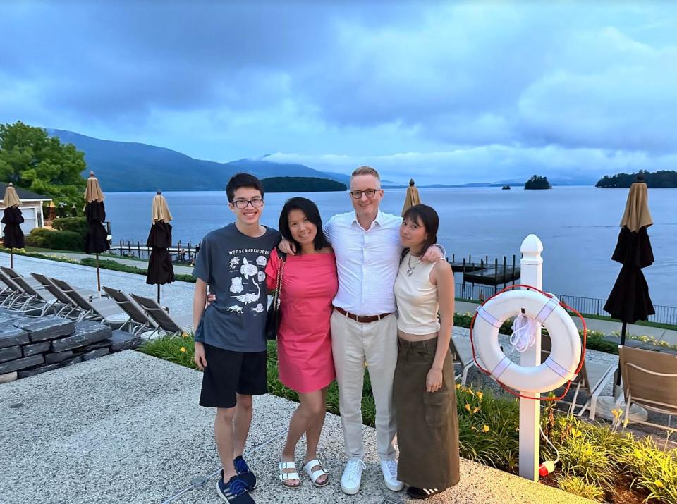 Ortiz standing next to her husband and two children in front of a body of water with mountains in the background.