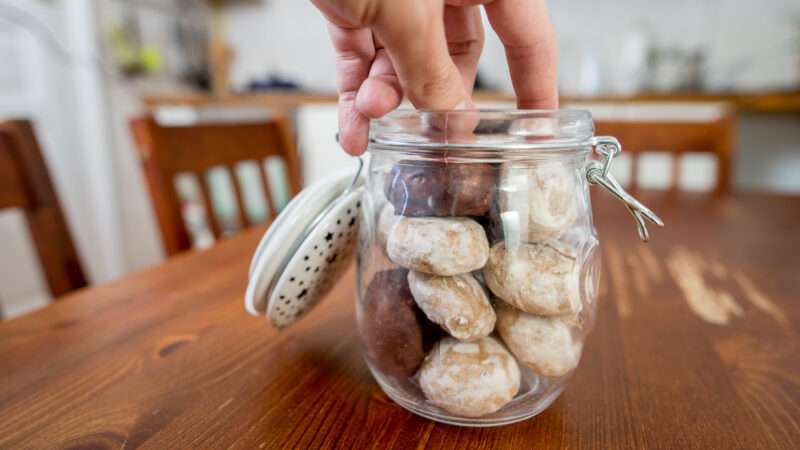 A hand reaches into a cookie jar to take a cookie.