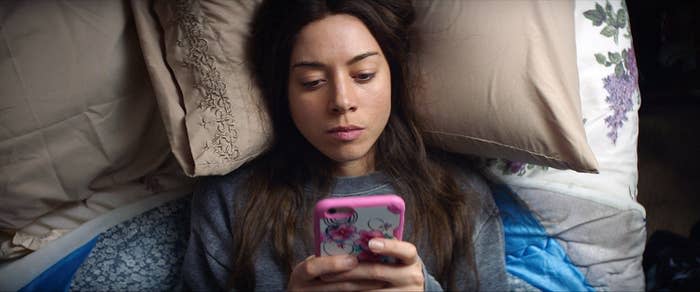 Ingrid laying in bed and looking at her phone in a scene from "Ingrid Goes West"