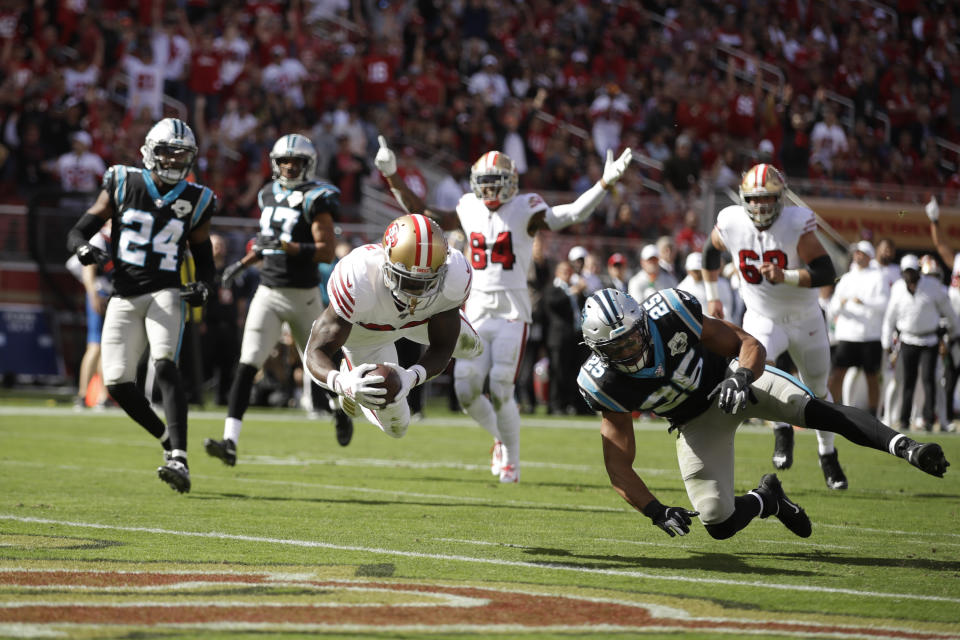 San Francisco 49ers running back Tevin Coleman goes diving into the end zone to score a touchdown as Carolina Panthers strong safety Eric Reid (25) and cornerback James Bradberry (24) look on during the first half of an NFL football game in Santa Clara, Calif., Sunday, Oct. 27, 2019. In the background is San Francisco 49ers wide receiver Kendrick Bourne (84). (AP Photo/Ben Margot)