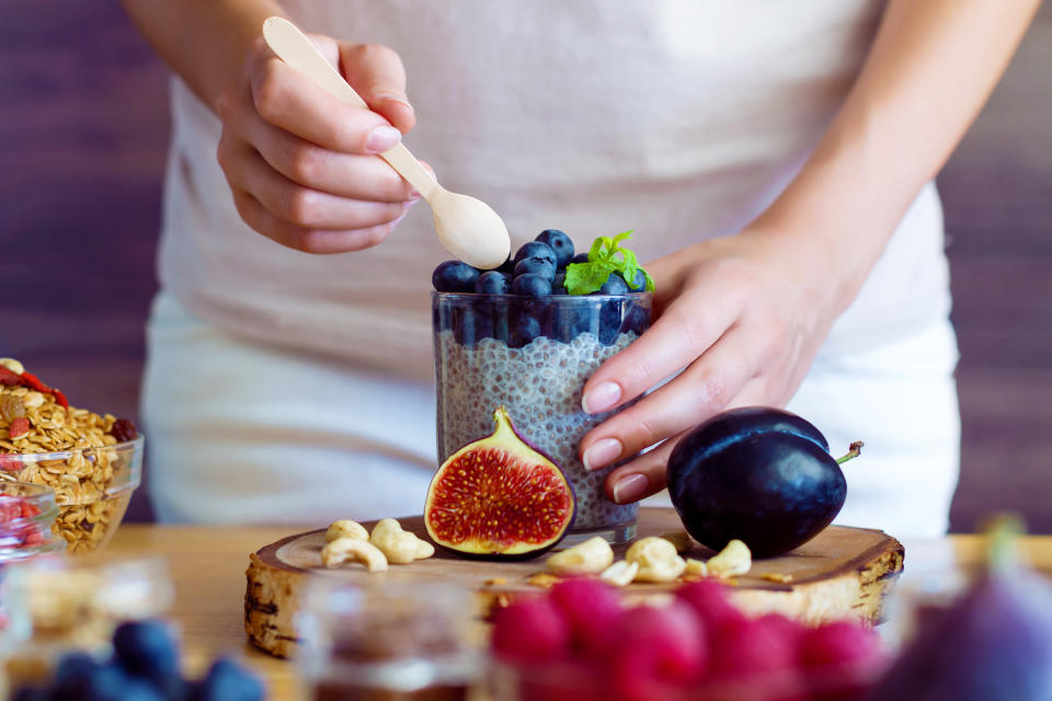 Female hands are preparing yogurt with chia and blueberries for good digestion, functioning of gastrointestinal tract. Summer berries, nuts, fruits, dairy products on table. Healthy food concept.